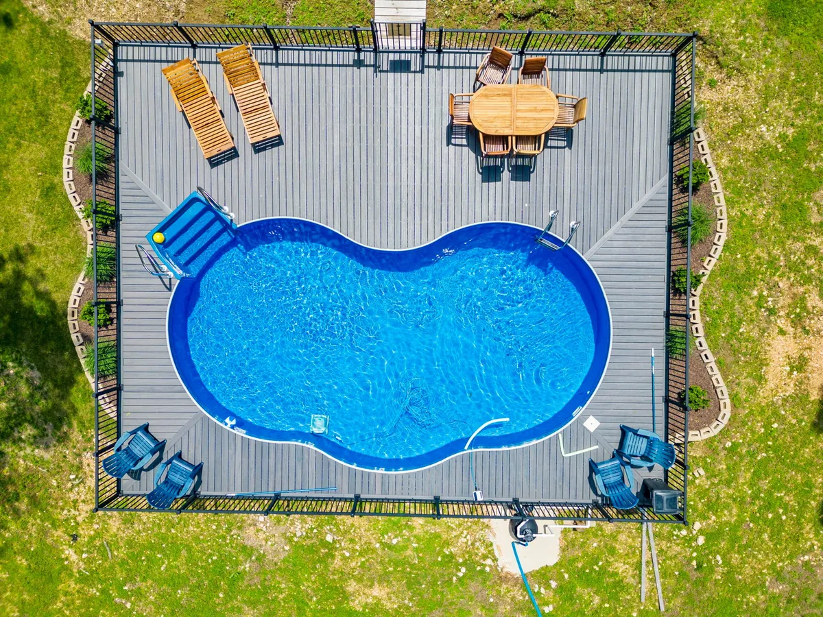 A welcoming exterior view with a sparkling saltwater swimming pool surrounded by a wooden deck, complete with lounge chairs and an outdoor dining table. The setting is bathed in natural light, evoking a sense of leisure and relaxation, ideal for swimming, sunbathing, and social gatherings. Lush trees provide a secluded, resort-style backdrop.