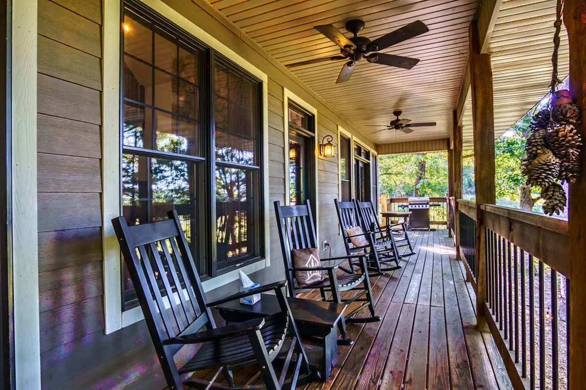 A welcoming front porch with rocking chairs, wooden railing, and an outdoor grill, offering views through large windows. The porch is set up for enjoying fresh air, relaxing with morning coffee, or hosting barbecues in a relaxed, communal atmosphere.