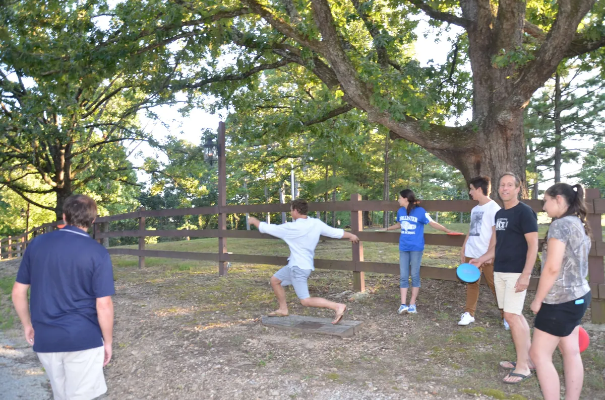 A group of people gathers beneath a large tree, engaged in playful outdoor activities. The setting suggests teamwork, games, and social fun in a relaxed, green environment, evoking the spirit of the estate’s custom treasure hunts.