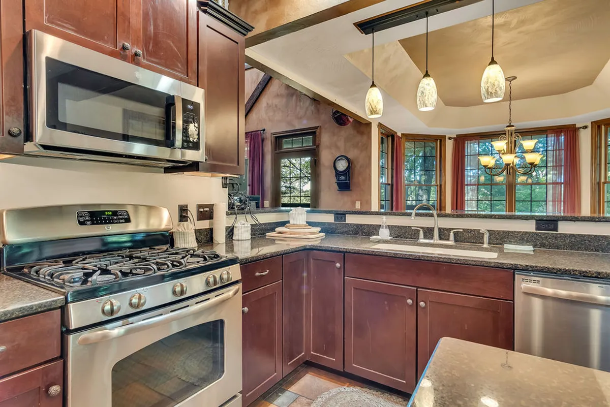 A chef’s kitchen adorned with granite countertops and rich wooden cabinetry, highlighted by stainless steel appliances and a prominent kitchen island. Large windows provide natural light, making the space bright and inspiring for culinary endeavors or casual gatherings.