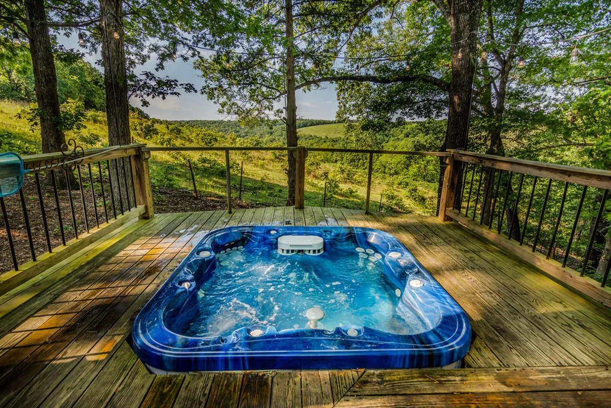 This exterior image features a hot tub set on a spacious deck, surrounded by lush greenery, creating a tranquil outdoor escape. The deck area is perfect for relaxing in the hot tub, enjoying nature views, stargazing at night, or hosting outdoor gatherings.