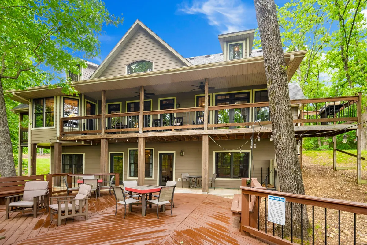 A spacious deck area with plenty of seating, a large upper balcony, expansive windows looking out onto natural surroundings, and space for group dining or outdoor activities. The scene radiates an inviting atmosphere for gatherings and outdoor fun.