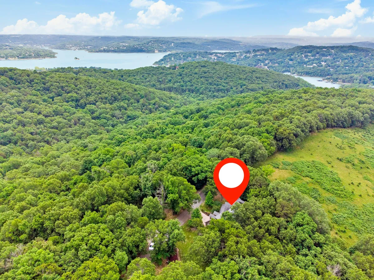 A serene exterior scene with lush greenery, a clear view of the lake, scenic rolling hills, and part of the house structure. The landscape invites thoughts of hiking, fishing, picnicking, and connecting with nature. The tranquil mood reflects the appeal of Table Rock Lake and the surrounding area.