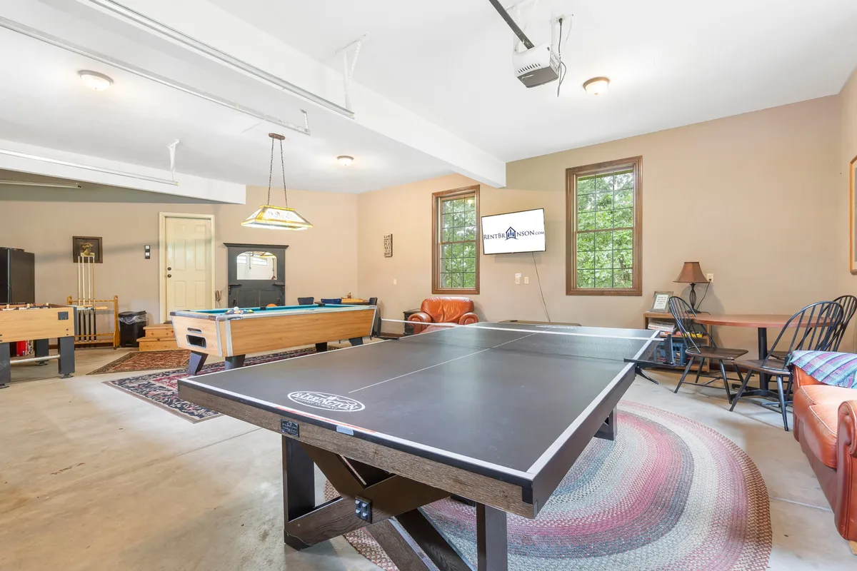 This image showcases a vibrant game room featuring a ping-pong table, pool table, foosball table, TV, and a comfortable seating area. The space is bright and designed for multiple group activities, emphasizing a casual, fun environment perfect for friendly competition and relaxation.
