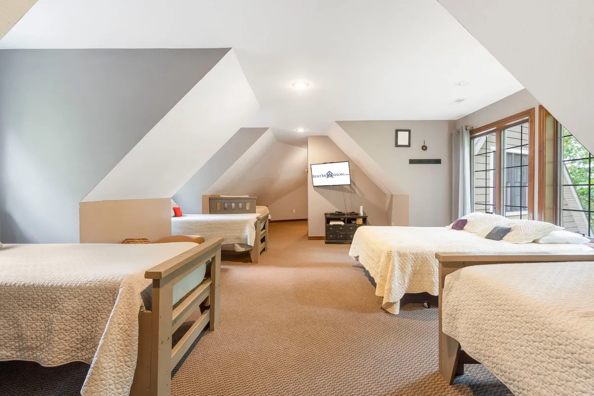 A cozy bunkhouse-style bedroom with three beds neatly arranged, a television, and large windows that fill the space with light. The room feels casual and welcoming—ideal for kids, cousins, or friends to unwind together.