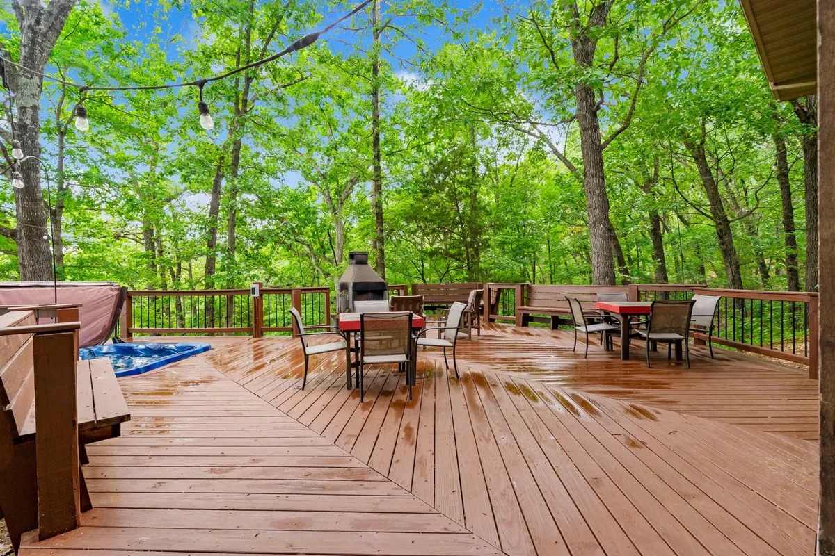 An inviting wooden deck with comfortable outdoor seating, a grill, and a hot tub, all nestled in a natural setting surrounded by trees. The deck is set up for both dining and relaxation, making it an ideal spot for gatherings, barbecues, or quiet mornings with coffee.