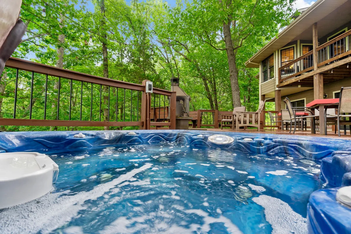 A tranquil outdoor deck area featuring a bubbling hot tub nestled among lush greenery. Stylish outdoor furniture invites relaxation, with space for social gatherings or quiet moments. The deck is positioned for immersive views of the natural surroundings, ideal for evening stargazing or afternoon lounging.