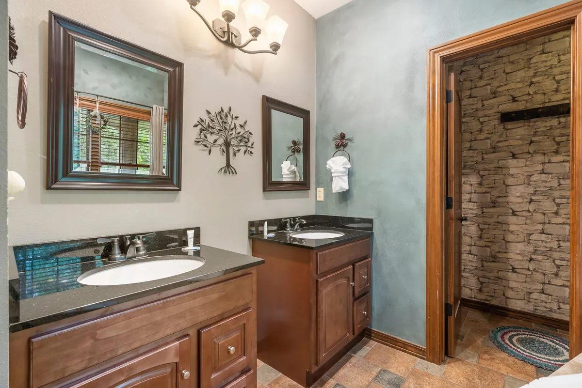 A modern, serene bathroom featuring double sink vanities, framed mirrors, decorative wall art, and a stone accent wall. The mood is calm and spa-like, suggesting plenty of space and high-end finishes for personal routines.