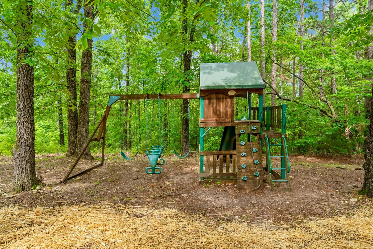 A vibrant outdoor play structure featuring swings and a climbing wall nestled among trees, with open space for children to play and families to gather. The setting is bright and joyful, capturing the energy of childhood adventures.