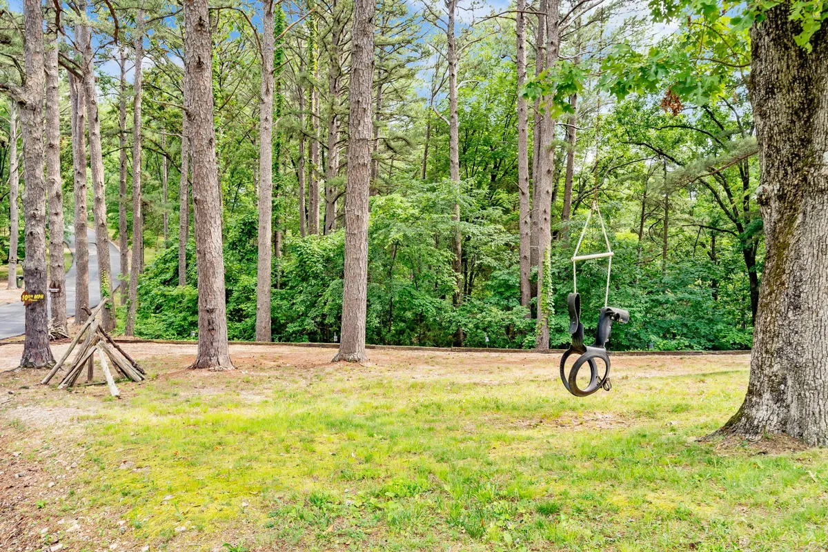 A playful exterior scene featuring a swing set nestled among tall trees and a cleared grassy area, offering a family-friendly setting for children to play or guests to picnic and explore the outdoors.