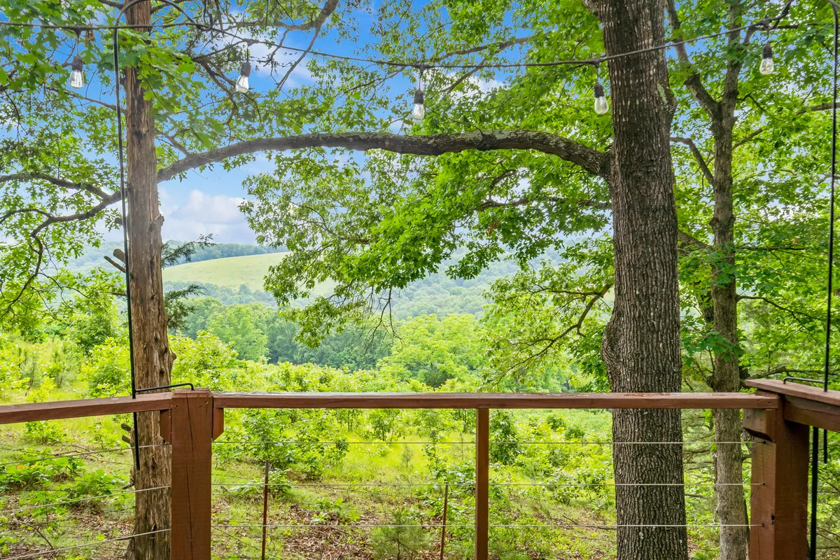An expansive view from a wooden deck, overlooking lush meadows, distant hills, and forested landscape. The setting is tranquil and open, suggesting immersion in preserved nature and opportunities for relaxation or stargazing.