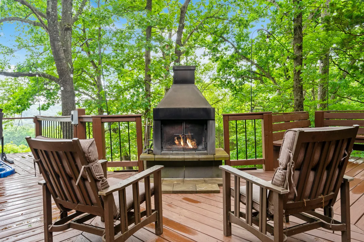 An inviting deck with a cozy outdoor fireplace surrounded by wooden chairs, set against a backdrop of vibrant greenery. The setup is perfect for enjoying sunset views, warming up on crisp evenings, or engaging in intimate conversations in a peaceful outdoor setting.